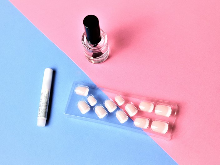 A box of press-on nails and nail glue on a blue and pink background