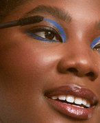 person wearing blue graphic eye makeup holding mascara wand up to eyelashes