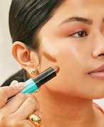 Person applying contour makeup to their cheekbone with NYX Professional Makeup Wonder Stick Contour and Highlighter Stick