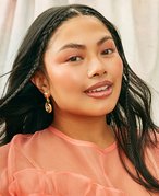 Picture of a model with black wavy hair and a peach colored blouse