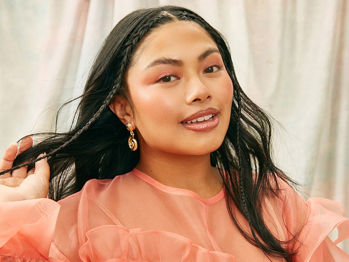 Picture of a model with black wavy hair and a peach colored blouse