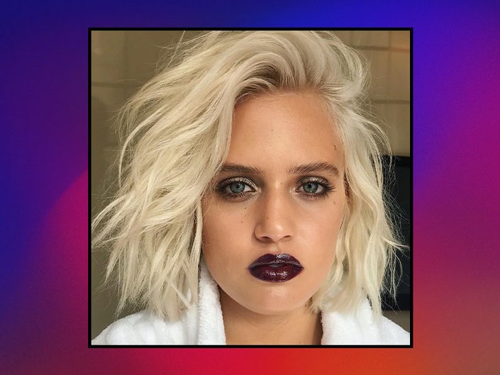 Picture of a platinum blonde model with smoky eyes and dark lipstick on red and purple gradient graphic background