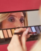 Person holding eyeshadow palette looking in the mirror 