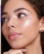 Close-up of a person in profile looking to the side of the camera with their hair pulled back and three dots of highlighter on their cheeks not blended in