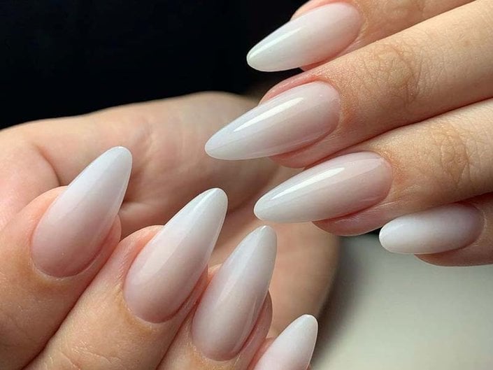 Close up of long, oval-shaped nails painted with milky neutral polish