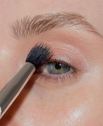 Close-up photo of a model blending a transition shade in her crease
